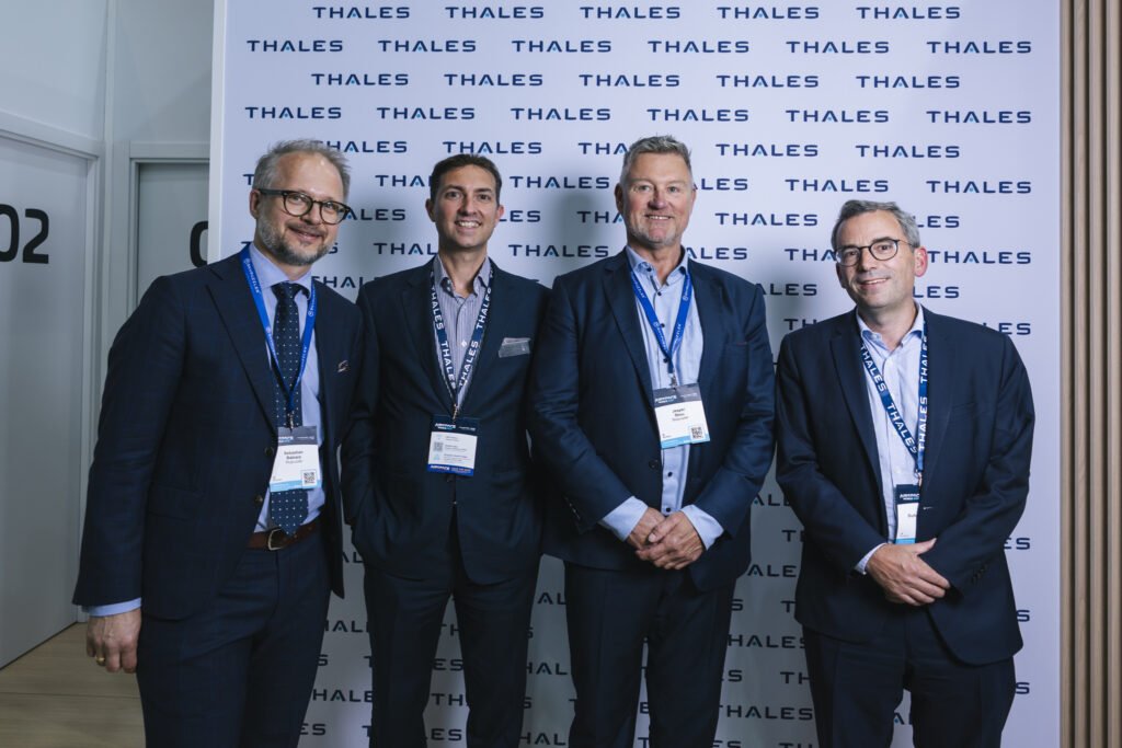 Four males all wearing blue suits and blue keyhangers around their neck standing next to each other and smiling