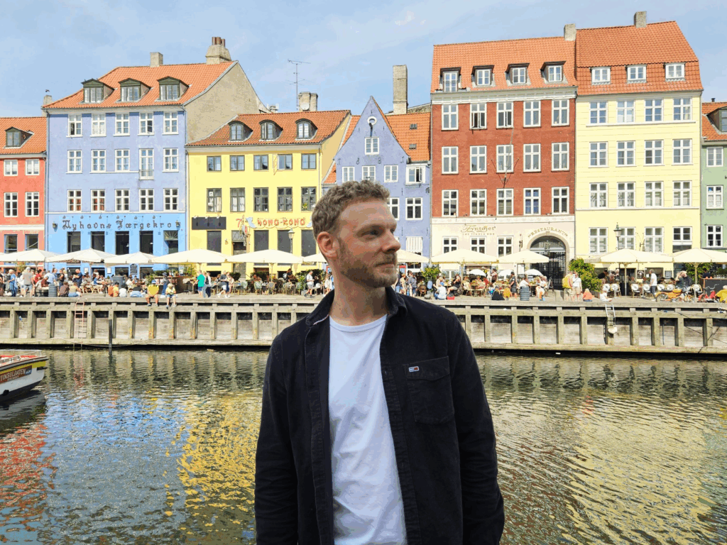 Male standing in front of water and colorful buildings