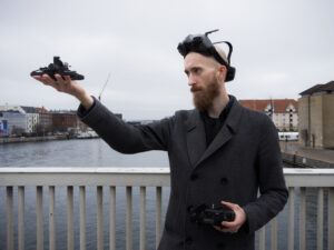 Male with beard holding drone in one hand and controller in other hand
